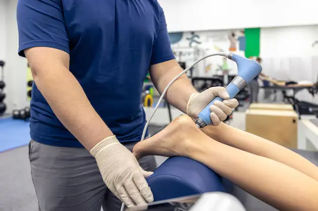 A clinician in gloves treats the sole of a patient's foot with a handheld device