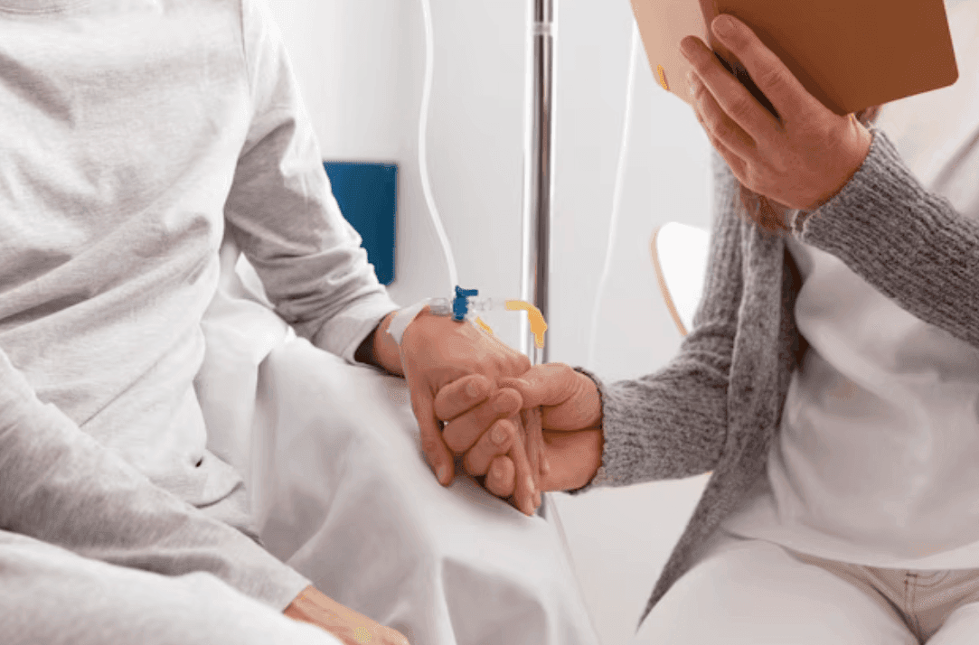 A patient receiving an iron infusion holds hands with a support person at the bedside.